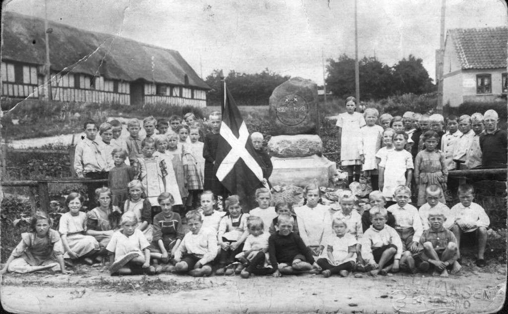 1920. Byens børn bliver fotograferet ved den nye mindesten. Siden blev der holdt fest ved vandmøllen. Til venstre ses tvillingegården Borum Højgård og den unavngivne gård, der senere fik navnet Storkesiggård. Til højre huset Bysvinget 2.